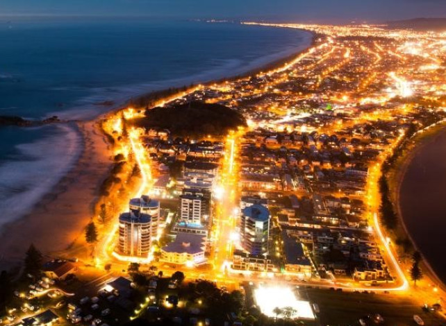 View of a beachside town at night lit up by lights on streets and in buildings. 