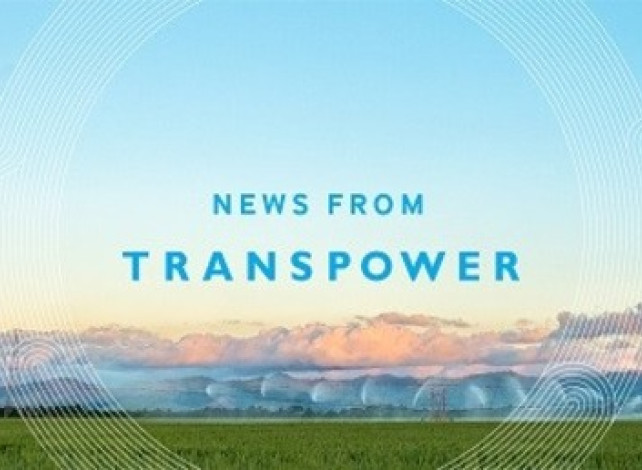 Image of a transmission tower with lines coming from it in a wide green field with the sunrise behind it.