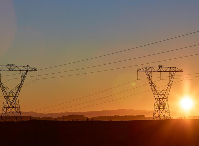 Image of two transmission towers during sunset with the sun going down just beside one of the towers.