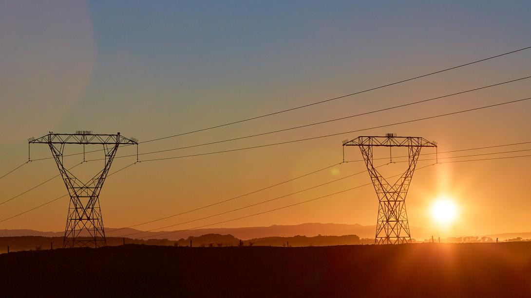 Image of two transmission towers during sunset with the sun going down just beside one of the towers.